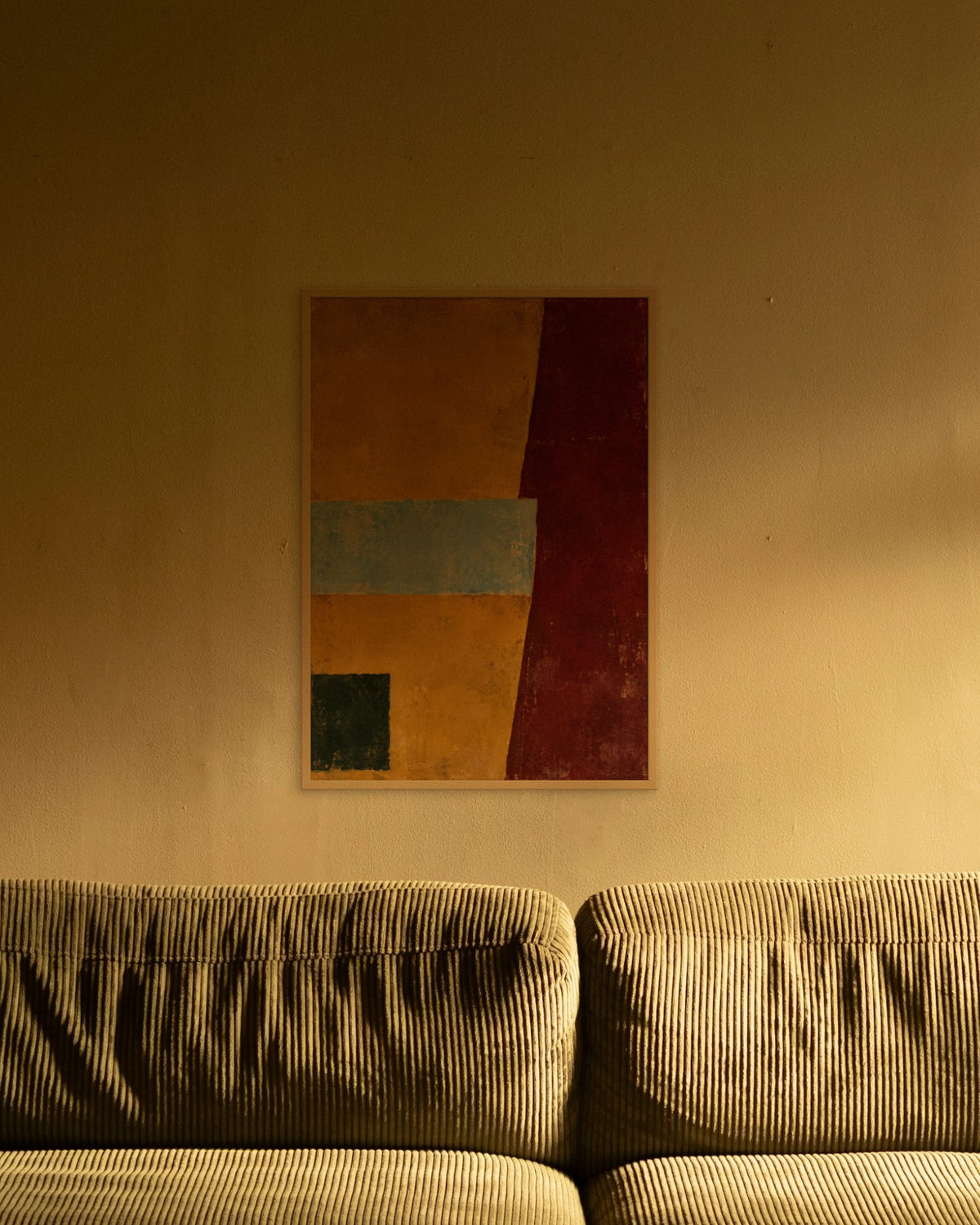 Amber Horizon art print in a natural oak frame above an olive corduroy sofa lit by a warm lamp