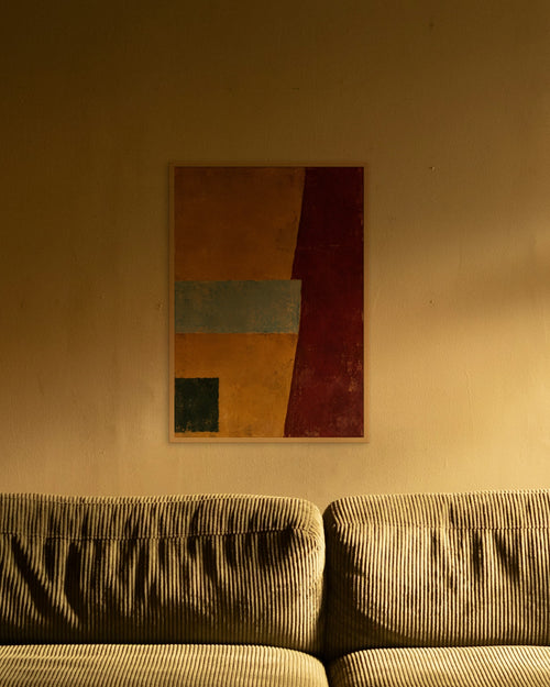 Amber Horizon art print in a natural oak frame above an olive corduroy sofa lit by a warm lamp