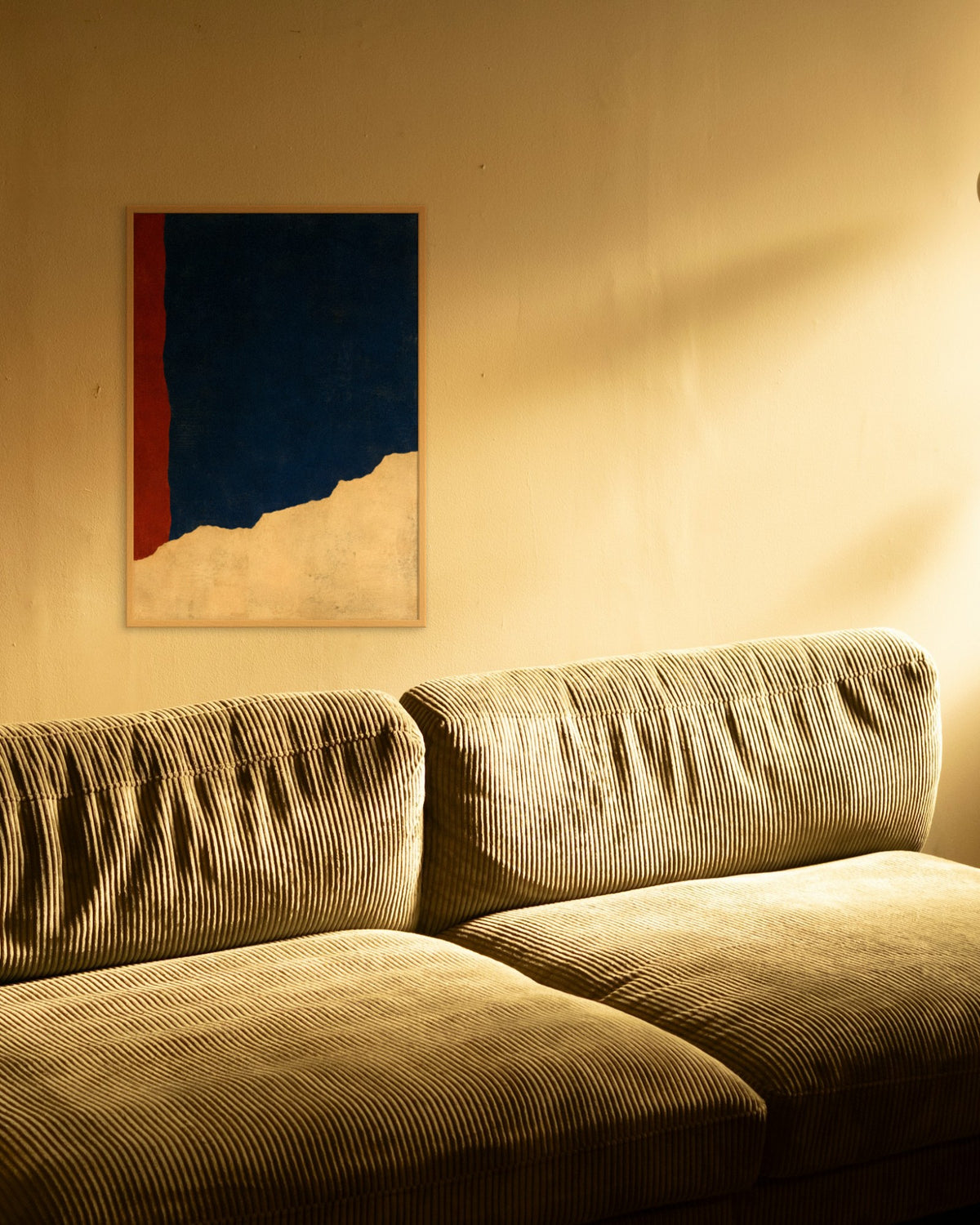 Cobalt Ridge art print in a natural oak frame above an olive corduroy sofa in warm evening light