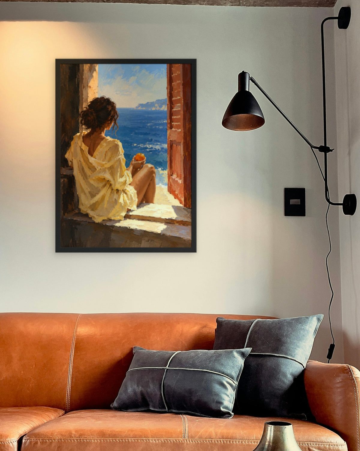 Orange by the Sea art print in a black frame above a cognac leather sofa beside a black wall lamp