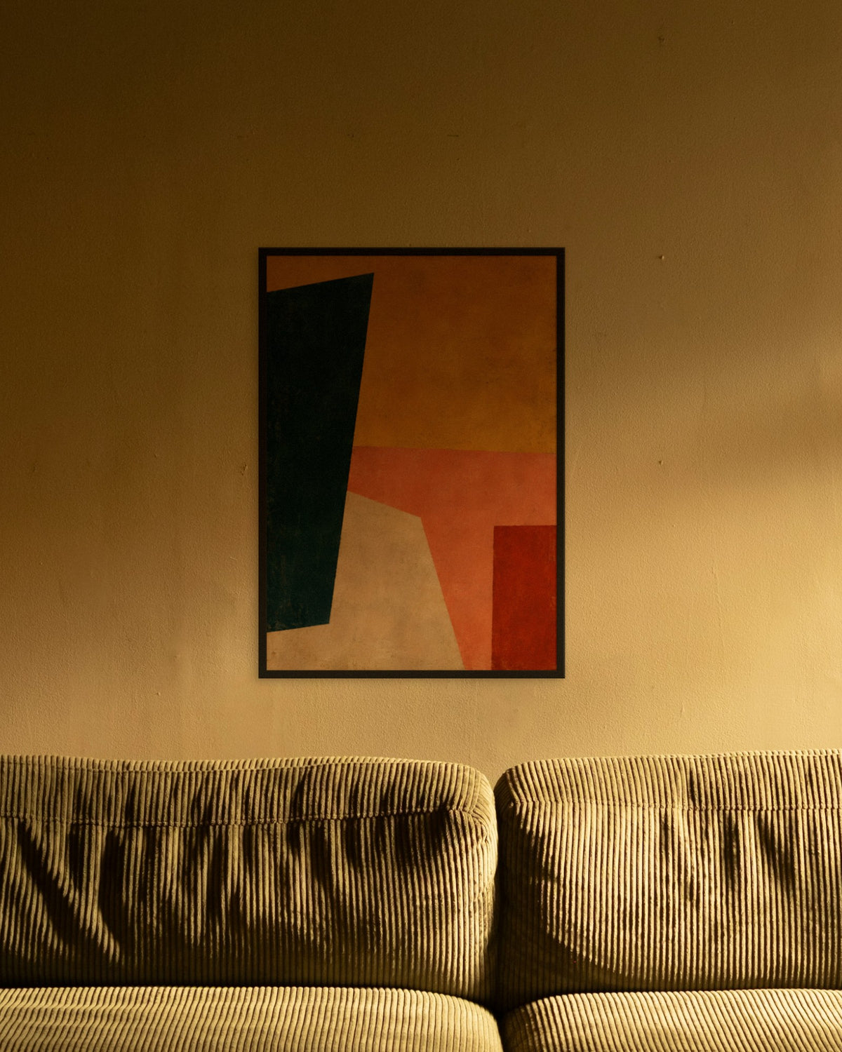 Saffron Composition art print in a black frame above an olive corduroy sofa lit by a warm lamp