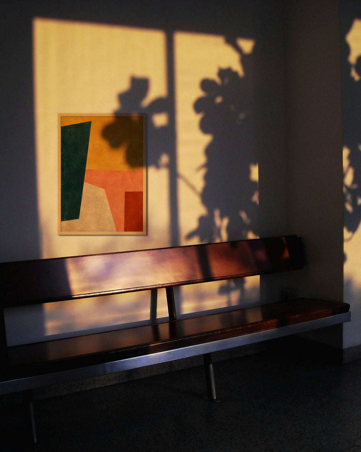 Saffron Composition art print in a natural oak frame on a sunlit wall with plant shadows above a wooden bench