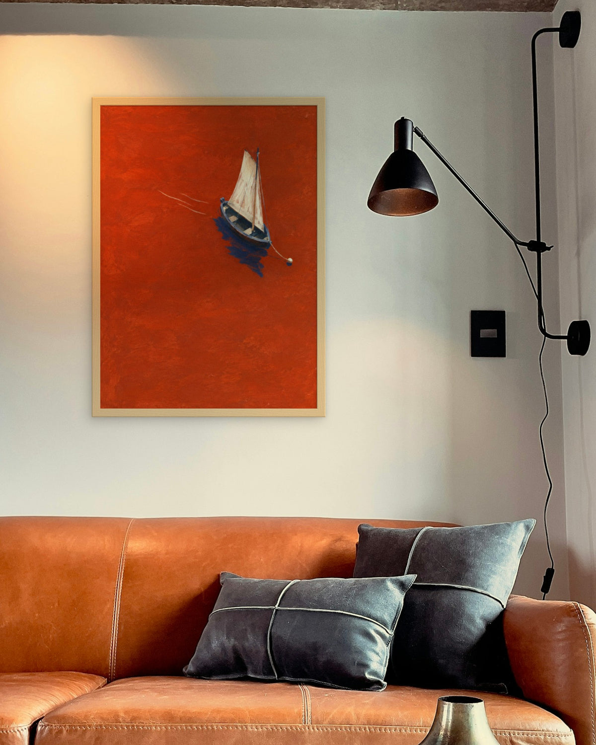Vermilion Sail art print in a natural oak frame above a cognac leather sofa beside a black wall lamp